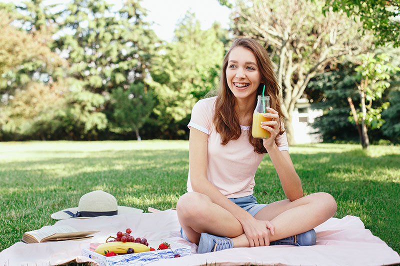 smiling girl with braces holding orange juice at a picnic