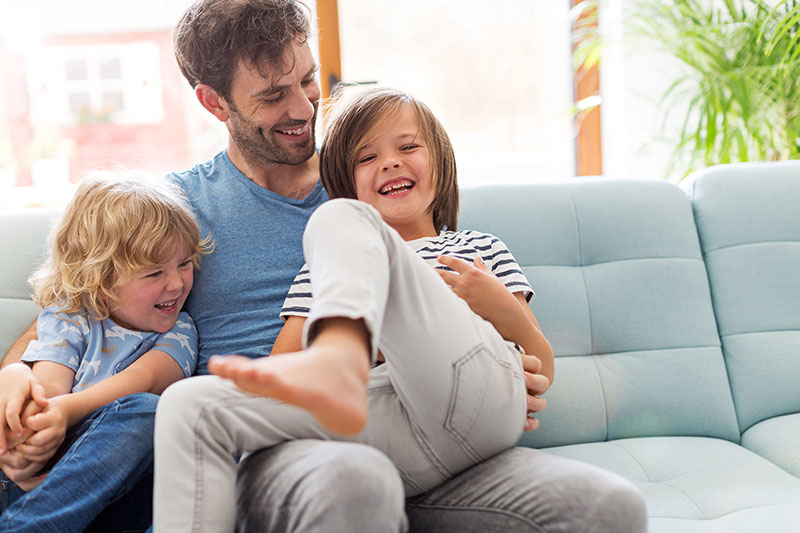 father with two laughing kids on a blue couch